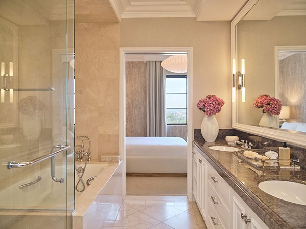 Maybourne Beverly Hills Residence Bathroom: A white and marble sink and pink flowers sits to the right. A mirror sits above the sinks. To the left is a bath and shower.