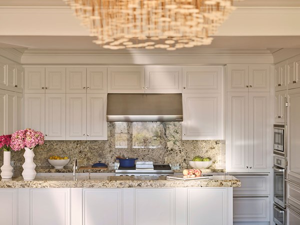 Maybourne Beverly Hills Residence Kitchen: A white kitchen with a marble counter top. Two white vases with pink flowers sits to the left. In the centre there is a blue cooking pot. To the right there are peaches and a bowl of watermelons.